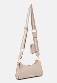 Sac bandoulière beige avec fermeture éclair et accessoires dorés, bandoulière réglable beige et blanche rayée, et petite pochette attachée.