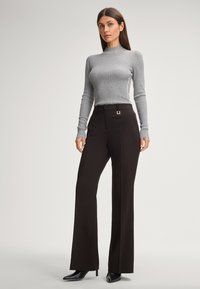 Grijze geribbelde coltrui met lange mouwen, gecombineerd met zwarte wijde broek met een riemlus en vierkante gespdetail, vergezeld van zwarte hoge hakken.