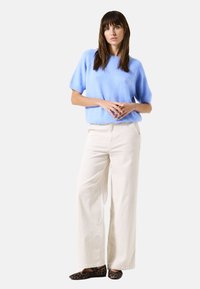 Pull court bleu clair à manches courtes en tissu doux, associé à un pantalon large crème et des ballerines imprimé léopard. Vue de face, fond neutre.