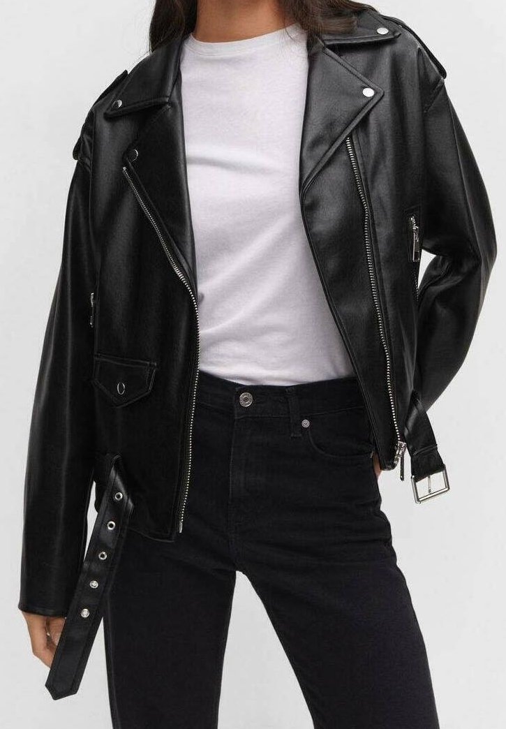 Femme portant une veste de motard noire en cuir synthétique sur un t-shirt blanc et un jean noir taille haute, sur un fond uni.