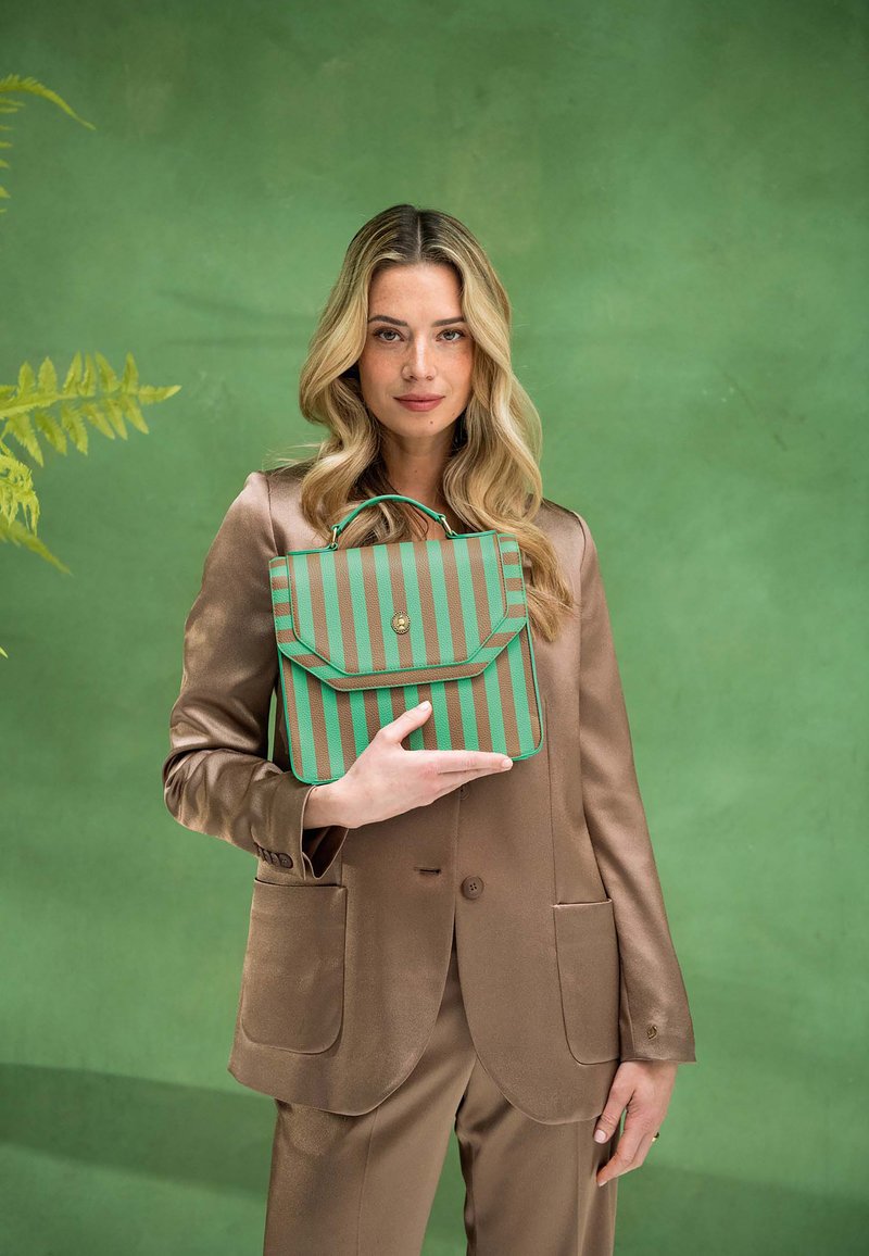 Grüne und braune gestreifte Handtasche mit einem Klappenverschluss und goldenem Zubehör, gehalten vor einer Person in einem satinierten braunen Anzug vor einem grünen Hintergrund.