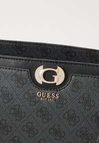 Black textured handbag made of synthetic material, featuring a gold logo clasp and "GUESS EST 1981" embossed on the front.