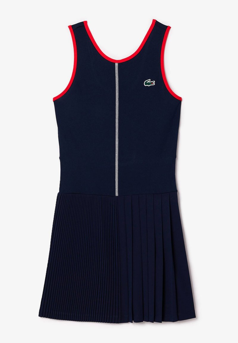 Marineblauwe mouwloze jurk met geplooide rok, contrasterende rode biezen bij de halslijn en armopeningen, voorzien van een centrale zilveren ritssluiting en geborduurd logo.