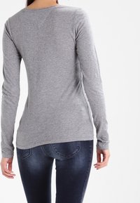 Top gris de manga larga con cuello redondo y diseño ajustado, fabricado en un tejido suave. Detalle de costura visible en las costuras de los hombros.