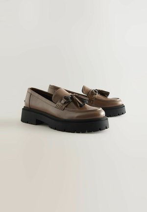 Brūni ādas mokasīni ar melniem masīviem platformu zole, ar pušķu akcentiem un gludu tekstūru. Klasisks dizains ar mūsdienīgu pieskārienu.