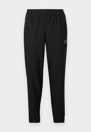 Zwarte sportbroek met een gestructureerde stof, elastische taille, trekkoord, taps toelopende pijpen en een klein gouden logo aan de linkerkant.