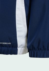 Veste bleu marine avec un panneau blanc contrastant, un tissu texturé, des poignets élastiques et un logo étiqueté "AEROREADY" en bas.