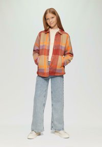 Geruite flanellen shirt in tinten van rood, oranje en beige, met grote zakken en knoopsluiting, gecombineerd met lichtblauwe wijde jeans.