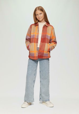 Geruite flanellen shirt in tinten van rood, oranje en beige, met grote zakken en knoopsluiting, gecombineerd met lichtblauwe wijde jeans.