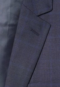 Tissu bleu foncé avec un motif à carreaux comportant de fines lignes violettes, surface texturée et un design rayé lisse sur la gauche.