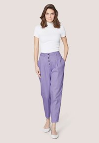 Licht paarse high-waisted broek met een rechte pasvorm, voorzien van vijf zwarte knopen aan de voorkant en zijzakken. Gemaakt in combinatie met een wit getailleerd topje.