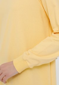 Camisa de manga larga de suave algodón en un amarillo claro con puños acanalados y un corte relajado, que presenta una textura suave y detalles de diseño mínimos.