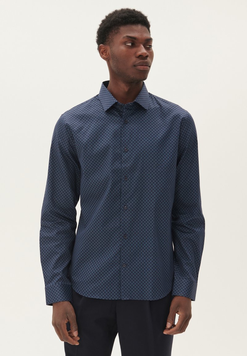Camisa de patrón azul marino con cuello abotonado, mangas largas y un diseño geométrico. Fabricada en una tela suave con un corte ajustado.