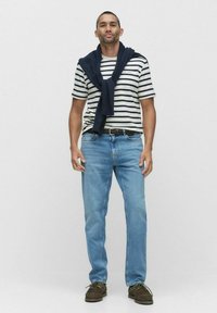 Stribet kortærmet skjorte i marineblå og cremefarvet, parret med lyseblå jeans og brune casual sko, med en marineblå sweater draperet over skuldrene.