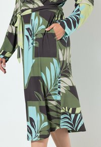Sukienka w kwiatowy wzór w kolorach zielonym, czarnym i jasnoniebieskim, z wiązanym paskiem, długimi rękawami i bocznymi kieszeniami. Gładka faktura materiału.
