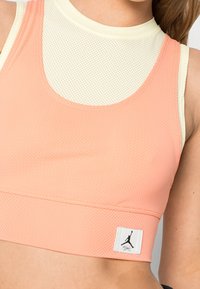 Stanik sportowy wykonany z lekkiej, oddychającej siateczki w kolorze koralowym i jasnym żółtym. Zawiera metkę z logo na brzegu i dopasowany krój.