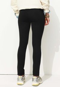Leggings noirs avec une coupe slim, une texture lisse et une taille haute, associés à des chaussures de sport argentées et jaunes.