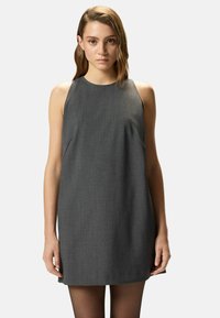 Vestido gris sin mangas con escote redondo, silueta recta, textura suave y detalles en los paneles laterales. Se lleva con medias negras transparentes.