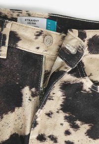 Beige Mittelhoch geschnittene gerade Jeans mit schwarzem Spritzmuster. Ausgestattet mit silbernem YKK-Reißverschluss und Metallknopf, mit Etikett, das Größe und Herkunft angibt.