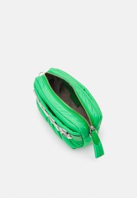 Borsa trapuntata verde con zip argentata, caratterizzata da una texture liscia e un accento di catena chunky sul davanti. Aperta, rivela un interno beige.