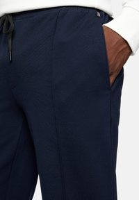 Navy blue jogger pants made of soft fabric, featuring side pockets, elastic waistband with a drawstring, and subtle stitching details.