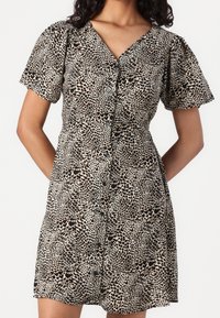 Robe à boutons jusqu'aux genoux avec un col en V, des manches courtes bouffantes, et un motif léopard beige et noir.