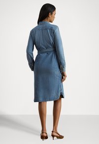 Džinsa krekla kleita ar garām piedurknēm, jostu viduklī un sānu šķēlumiem. Gaiši zils audums ar maigu tekstūru un pogājamiem aproču galiem.