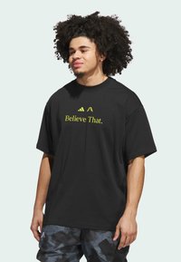 Sort kortærmet t-shirt med teksten "Believe That." i neongul skrift; afslappet design og rund hals.