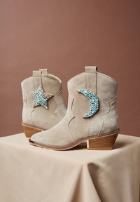 Stivaletti beige in camoscio dal design curvo, con decorazione a stella e mezzaluna in gemme turchesi e trasparenti, tacco impilato in legno.