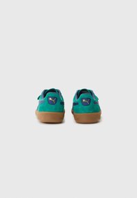 Gröna mockasneakers med blå accenter, gummisulor och en gyllene Puma-logotyp på hälen, med en låg profil och justerbara remmar.