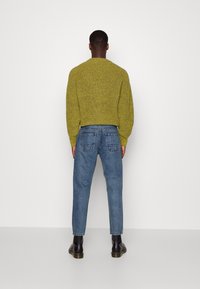 Zelený pletený svetr s texturovaným povrchem, doplněný světle modrými zúženými džíny. Černé kotníkové boty dokončují celý outfit.