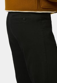 Zwarte broek van rekbare stof, met een enkele achterzak met knoopsluiting en een strak, recht model.