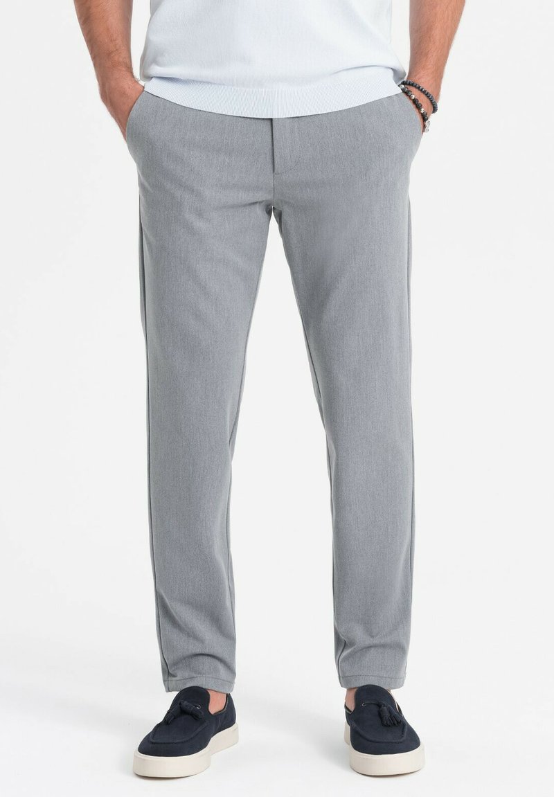 Helle graue Hosen mit glatter Textur, taillierter Passform, seitlichen Taschen und flachem Bund. Kombiniert mit dunkelblauen Slippern.