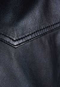 Schwarzes Kunstleder mit strukturierter Oberfläche. Sichtbare Nähte und ein gefaltetes Ecken-Detail. Glänzende, glatte Oberfläche und robuste Erscheinung.