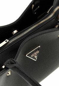 Borsa a tracolla in pelle nera con finitura testurizzata, zip dorata e accento del logo metallico triangolare sul davanti.