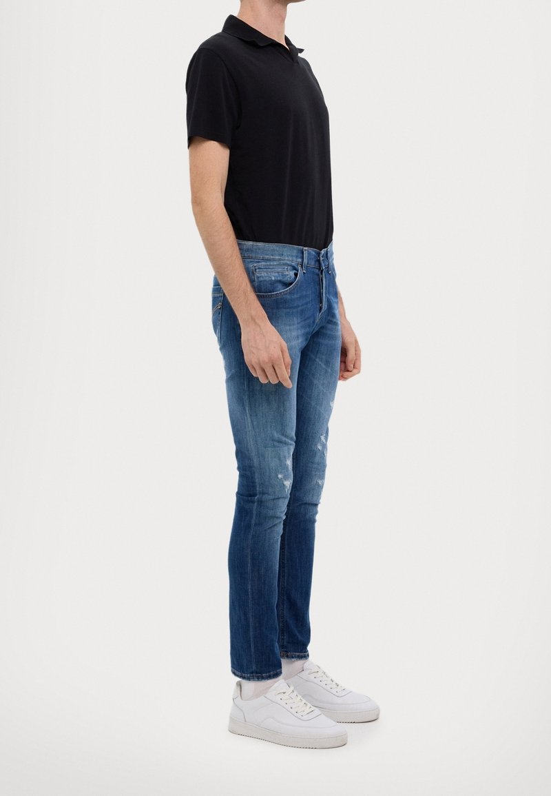 Svart polo skjorta, blå slitna jeans och vita sneakers. Tight passform och rak benform med subtila blekningar på denim.