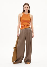 Débardeur orange à côtes associé à un pantalon large beige. Porte un sac fourre-tout marron et des chaussures slip-on marron clair.