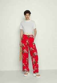 Calças largas florais vermelhas com folhas verdes, apresentando uma cintura alta e uma camisa branca de mangas curtas. Usadas com sandálias de plataforma.