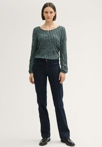 Dunkelblaue Jeans aus Denim, kombiniert mit einem langärmligen Oberteil in grünen Streifen, das über einen runden Ausschnitt und einen Knopfdetail an der Vorderseite verfügt.