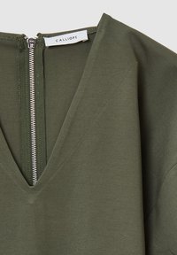 Top verde oliva realizzato in tessuto liscio, con scollatura a V profonda e zip argentata sul retro; presenta dettagli di cucitura angolari.