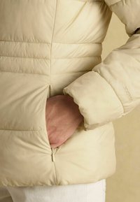 Svetlofialová puffa bunda s prešívaným vzorom, bočné vrecko so zipsom a elastické manžety. Hladká, lesklá textúra.