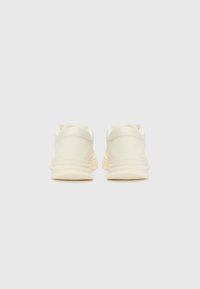Cream-colored sneakers with a smooth, matte finish, featuring a rounded shape, padded collar, and textured rubber sole.
