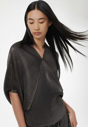 Metallic grey top with a loose fit, featuring a deep V-neck, ribbed texture, and short sleeves. Accented by fluttering fabric and pleated details.