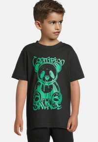 Juodas medvilninis marškinėliai su žaliu grafiku, vaizduojančiu lašančią meškiuką su tekstu. Trumpomis rankovėmis, laisvos formos ir kasdienišku dizainu.