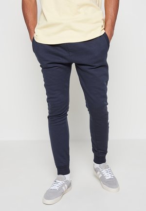 Navy Jogginghosen aus einem weichen Stoff, mit einem taillierten Design, elastischem Bund und Seitentaschen. Kombiniert mit grauen Sneakers.