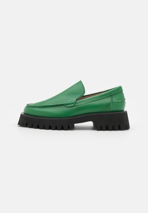 Mocasines de cuero verde con punta redonda, costuras elevadas y una suela gruesa de goma negra con ranuras texturizadas.