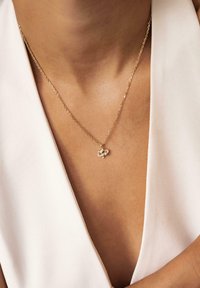 Gold chain necklace featuring a delicate, abstract pendant with small spherical accents. Necklace rests on a bare neck against a light fabric.