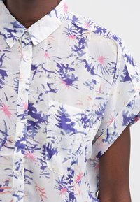 Koszula z krótkim rękawem, zapinana na guziki, wykonana z lekkiego, przezroczystego materiału w kolorowy kwiecisty wzór w odcieniach fioletu, różu i bieli. Posiada kieszonkę na piersi.