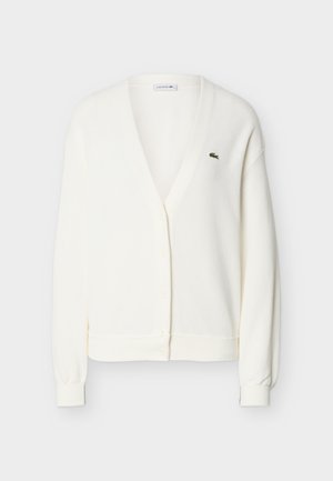 Cardigan blanc en tricot avec encolure en V, fermeture à boutons, manches longues, poignets côtelés, et petit logo crocodile vert sur le côté gauche de la poitrine.