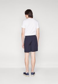 Marineblå shorts med elastisk talje og en baglomme. Sammen med en hvid t-shirt og blå sneakers med lyse såler.